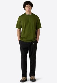 Olivgrünes kurzärmliges T-Shirt mit Rundhalsausschnitt und dem Logo "THE NORTH FACE". Kombiniert mit schwarzen Hosen und braunen Wanderschuhen.