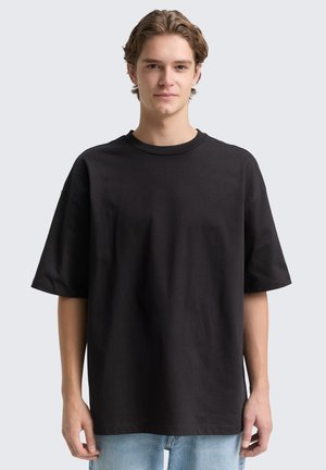 Black oversized t-shirt made of cotton. Features a rounded crew neckline and short sleeves. Fabric appears soft with a smooth texture.