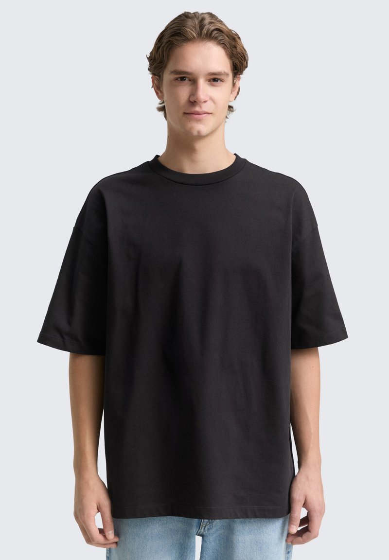 Fekete, oversized pamut póló. Kerek nyakkivágással és rövid ujjakkal rendelkezik. Az anyag lágy és sima tapintású.