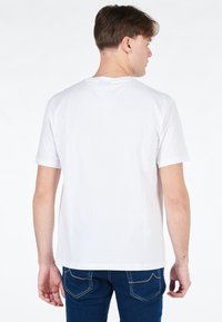 T-shirt bianca a maniche corte con scollatura a girocollo, caratterizzata da una texture liscia e un taglio dritto, indossata da una persona vista da dietro.