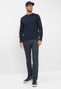 Marineblaues Langarmshirt mit Rundhalsausschnitt, kombiniert mit strukturierten dunkelblauen Hosen und marineblauen Sneakers. Als Accessoires wird eine passende Mütze getragen.