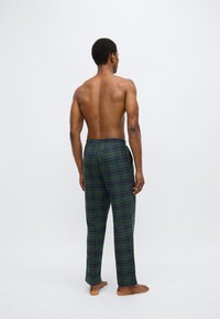 Ternet pyjamasbukser i mørkegrøn med lilla accenter, med elastisk talje og afslappet pasform. Stribet tekstur synlig.