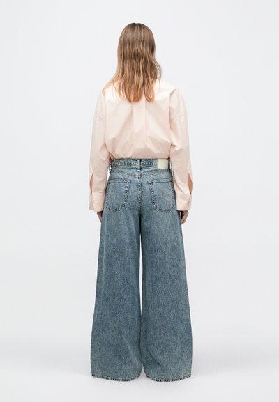 Hellrosa Langarmshirt mit gerafftem Rückendetail, kombiniert mit weit geschnittenen blauen Jeans aus Denim mit mittelhohem Bund und Taschen.