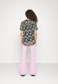 Tshirt preto transparente com padrão floral e mangas curtas, combinado com calças leves rosa claras, apresentando bainha arredondada e corte solto.