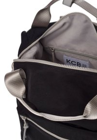 Bolsa negra con apertura con cremallera, interior gris y un pequeño bolsillo interior. Cuenta con correas de tela y una textura suave.