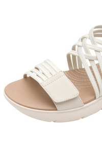 Sandalo in crema leggero con cinturini elastici incrociati, suola piatta beige e soletta testurizzata con motivi circolari.