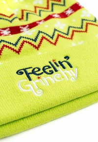 Berretto a maglia verde con motivi a zigzag in rosso e blu, con la scritta "Feelin' Grinchy" ricamata in blu e bianco.