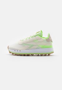 Chaussure de sport blanche et vert fluo avec un dessus texturé, une languette rembourrée et des pointes en caoutchouc sur la semelle pour une meilleure adhérence.