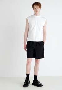 Top alba fără mâneci, pantaloni scurți negri, șosete negre și pantofi cu șireturi. Design simplu cu o croială lejeră. Material neted și croială dreaptă.