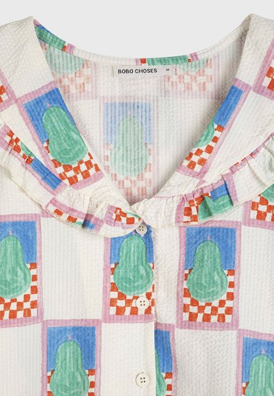 Blouse en tissu blanc texturé avec des imprimés de poires vert pastel à l'intérieur de carrés à carreaux roses et bleus, col à volants, et boutons blancs sur le devant.