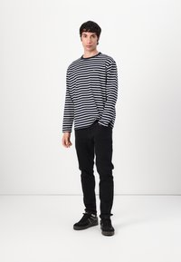 Stripet langermet skjorte i navy og hvit, mørke jeans og svarte sneakers. Skjorten har rund hals og en liten logo-detalj.