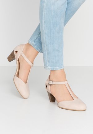 Beżowe skórzane sandały na obcasie w kształcie litery T, z teksturowanym paskiem wokół kostki, obcasem o wyglądzie naturalnego drewna oraz gładkim, zaokrąglonym noskiem.