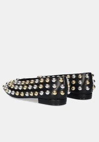 Zapatos planos negros con tachuelas metálicas en dorado y plateado, con puntera redonda y tacón bajo. Textura de cuero suave, diseño decorativo.
