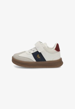 Zapatilla blanca con una raya azul marino y un logo dorado, acentos de ante gris, correa ajustable de Velcro y suela de goma marrón.
