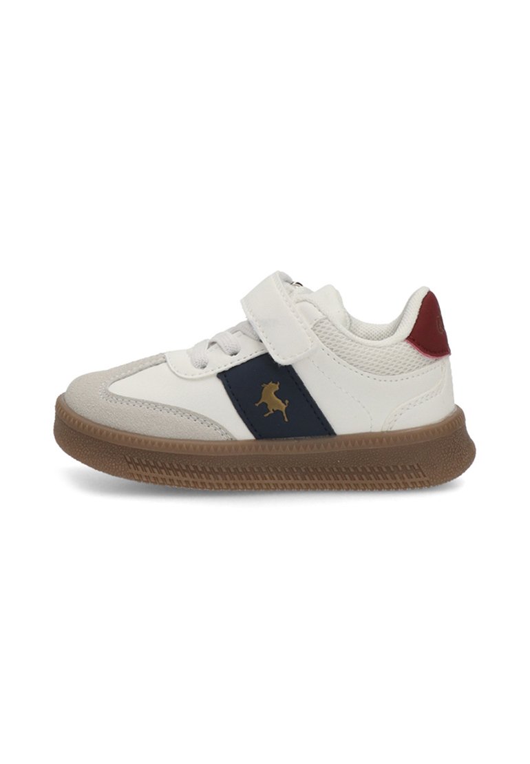 Zapatilla blanca con una raya azul marino y un logo dorado, acentos de ante gris, correa ajustable de Velcro y suela de goma marrón.