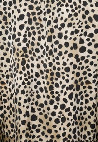 Tissu beige avec des taches imprimées léopard noires et brun foncé irrégulières, disposées selon un motif dense et dispersé.