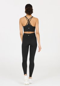Schwarzes sportliches Crop-Top mit überkreuzten Trägern und hochgeschnittenen Leggings, die aus strukturiertem Stoff hergestellt sind und ein Logodetail auf der Rückseite aufweisen.