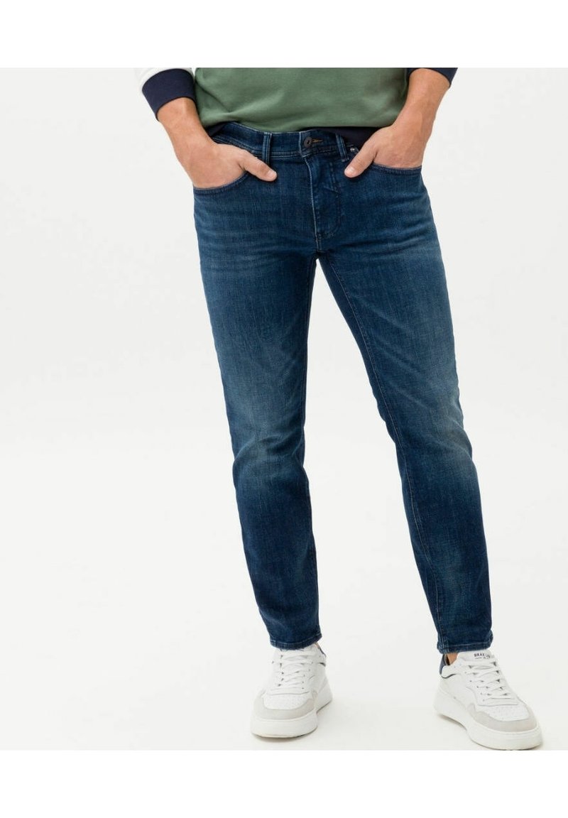 Dark blue denim jeans with a fitted design, five-pocket style, and stitch detailing. Worn with white sneakers for contrast.