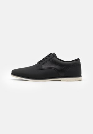Chaussures décontractées noires avec une tige à texture lisse, un design à lacets, un bout pointu, une semelle blanche contrastante et des accents de couture subtils.