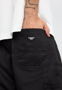 Černé cargo šortky vyrobené z odolné látky, se viditelnou kapsou a nášivkou ve tvaru srdce s nápisem "Carhartt WIP."