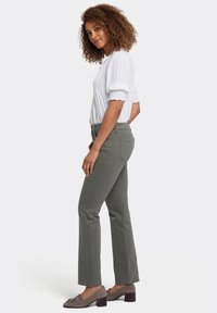 Pantalones rectos de color verde oliva, elaborados con un tejido texturizado, combinados con una blusa blanca de mangas abullonadas y escote redondo, usados con zapatos grises.