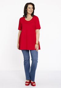 Rode tuniek met korte mouwen en een ronde hals, gecombineerd met lichtblauwe jeans en rode plateau-sandalen. Eenvoudige, relaxte silhoeet.