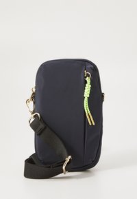 Sac bandoulière en nylon bleu marine de forme rectangulaire, avec des accessoires dorés et un tirette de fermeture éclair en paracorde verte fluo. Comprend une sangle noire ajustable.