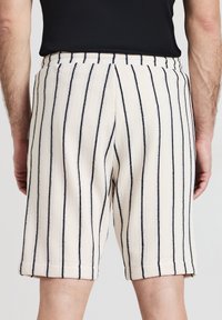 Un short à motifs beige clair doté de rayures verticales bleu marine et d'un tissu texturé, avec une taille élastique et des poches latérales.