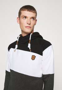 Hoody met zwart, wit en grijs kleurvlakken. Voorzien van gevlochten trekkoorden, bronzen accenten en een leren merkpatch.