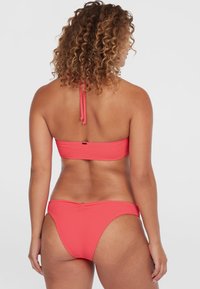 Koraal bikini set met een bandeau top en hoge uitsnijdingen aan de onderkant. Getextureerde stof met knoopbanden aan de achterkant. Geen versieringen of patronen.