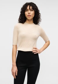 Hellbeiges, geripptes Strickoberteil mit kurzen Ärmeln und Rundhalsausschnitt, kombiniert mit hoch taillierten schwarzen Hosen; glatte Textur und figurbetontes Design.