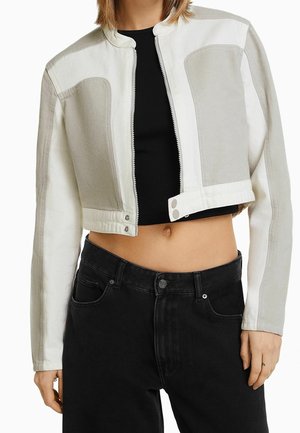 Gekürzte Jacke aus einer beigefarbenen und weißen Baumwollmischung, mit Stehkragen, Reißverschluss und kontrastierenden Panelelementen an Schultern und Ärmeln.