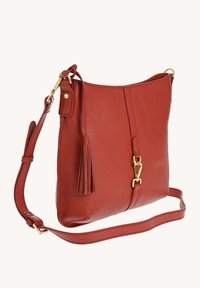 Sac bandoulière en cuir rouge avec une sangle réglable, fermoir en ton doré et un pompon décoratif sur le devant, présenté sur un fond uni.