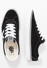 Black Vans sneakers with white laces and logo, featuring suede material and a white rubber sole, displayed on a white background.