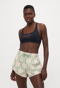 Black sports bra with "ROXY" logo in red, paired with green patterned shorts featuring pink flowers and a drawstring waistband.