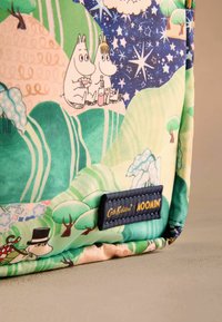 Többszínű anyagtáska Moomin karakterekkel, zöld dombok között, kék éjszakai égbolttal csillagokkal, valamint sötétkék címkével, amelyen az "Cath Kidston Moomin" felirat szerepel.