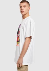 Hvid bomulds t-shirt med livligt grafisk print, der inkluderer tekst og illustrationer, korte ærmer og en afslappet pasform.