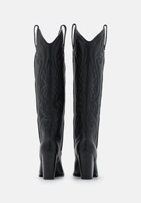Botas negras de cuero hasta la rodilla con diseño bordado, puntas afiladas, superficie texturizada y tacones de bloque. Presentan tiradores en los laterales.