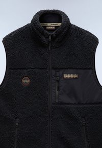 Black fleece vest with a high collar, featuring a textured, fluffy exterior and smooth fabric accents. Includes zippered pockets and logos.