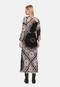 Lungo abito nero con un motivo paisley in rosa e bianco, caratterizzato da maniche lunghe e un design con schiena scoperta. Indossato con stivali neri.