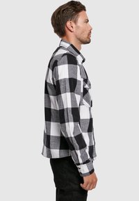 Zwart-witte geblokte flanellen shirt met een knoopsluiting kraag en lange mouwen, voorzien van patchzakken en een rechte snit.