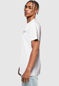 Hvid bomulds T-shirt med korte ærmer, der har et trykt logo i sort. Lige snit og blød tekstur, båret med lyseblå jeans.