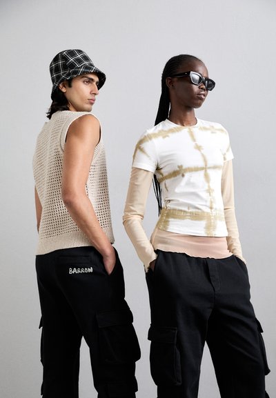 Top beige senza maniche a maglia, cappello a secchiello a quadri neri e pantaloni cargo con logo "BARROW"; camicia bianca con tie-dye sovrapposta a maniche lunghe beige.