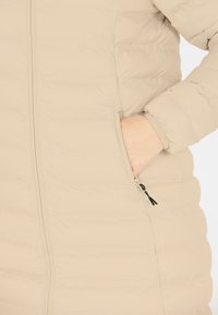Beige pufferjakke med vandrette sømme, lynlåslommer i siden og elastiske manchetter. Glat tekstur og isoleret design for varme.