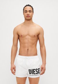 White swim shorts with black lettering "DIESEL" and tagline. Features drawstring waist and smooth fabric texture.