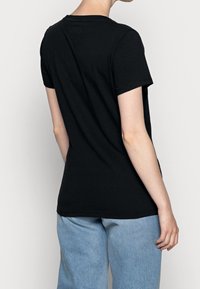 Svart bomulls t-shirt med korta ärmar, rund hals och en avslappnad passform. Baksidan har en enkel design, som är kombinerad med ljusblå byxor.