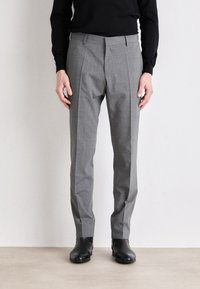 Pantaloni grigi su misura con un motivo testurizzato, dotati di pieghe laterali e vestibilità slim. Indossati con stivali neri alla caviglia.