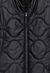 Veste matelassée noire avec motif ondulé, dotée d'une fermeture éclair complète et d'un tissu texturé. Matériau léger et résistant à l'eau.