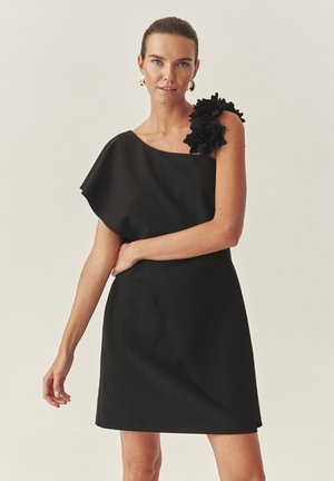 Zwarte jurk met asymmetrisch ontwerp met één schouder, voorzien van een rimpelbloemaccent, een gladde textuur en een jurk tot op de knie.