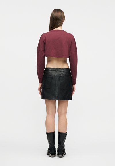 Γυναίκα με μακριά ίσια μαλλιά που φοράει ένα κοντό μπουφάν μπορντό, μαύρη δερμάτινη μίνι φούστα και μαύρες μπότες μέχρι τη μέση της γάμπας με αλυσίδες, γυρισμένη πλάτη.